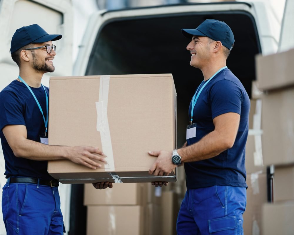 Happy manual worker cooperating while carrying cardboard boxes in a delivery van.